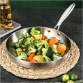 Uncoated stainless steel frying pan with roasted vegetables on a woven placemat