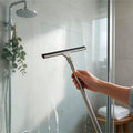 Stainless steel squeegee clearing a glass shower screen